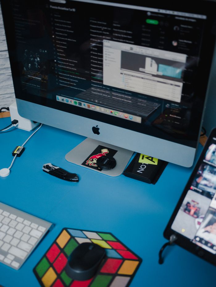 Service A neat workspace setup with computer, gadgets, and a Rubik's cube on a blue desk.